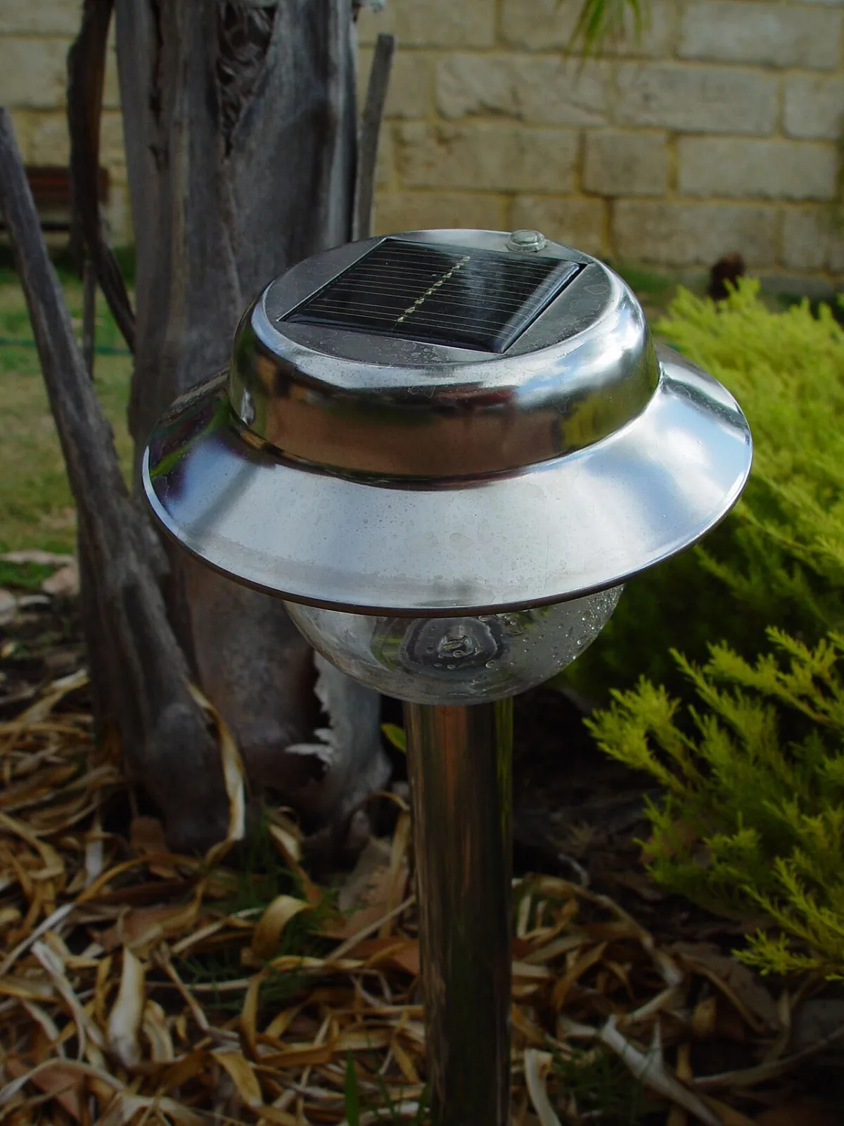 Solar tuinlamp op stok met zonnepaneel bovenop, geplaatst tussen struiken in een tuin